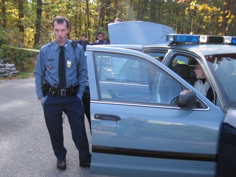 2001 Ford Crown Victoria - Police officer stands next to a Ford Crown Victoria police car with its hood and driver's door open.