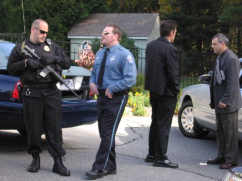 2001 Ford Crown Victoria - Law enforcement officers and civilians converse near parked cars on a residential street.