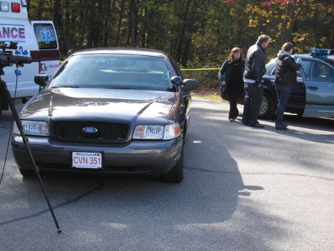 2001 Ford Crown Victoria - A police car is parked on a street with people and an ambulance nearby.