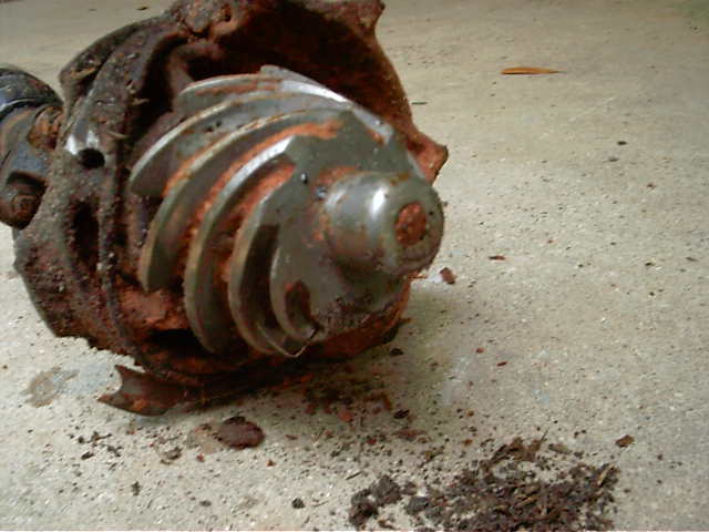 Broken rusty gearbox on concrete with cracked housing exposing worn worm gear