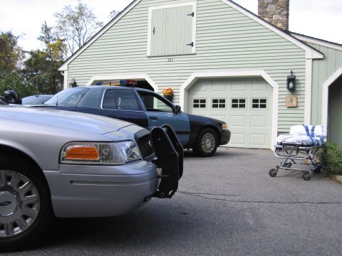 2001 Ford Crown Victoria - A silver 2001 Ford Crown Victoria police car is parked in front of a garage, with another police car behind it.