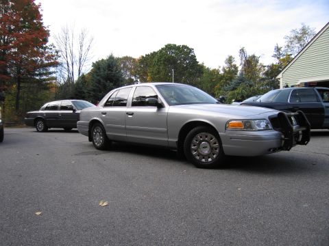 2001 Ford Crown Victoria - Two Ford Crown Victorias are parked in a driveway on an overcast day with trees in the background.