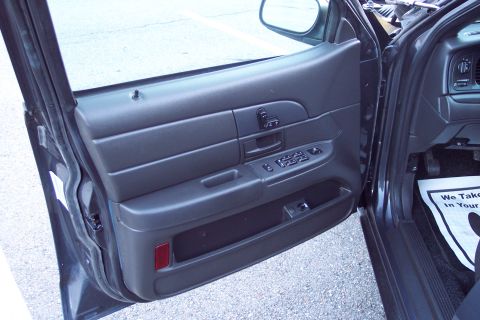 2001 Ford Crown Victoria - View of the interior door panel and dashboard, showing the power window controls and a floor mat with text.