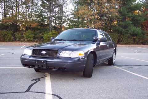 2001 Ford Crown Victoria - A dark gray Ford Crown Victoria is parked in an empty lot with trees in the background.