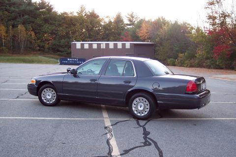 2001 Ford Crown Victoria - A dark gray 2001 Ford Crown Victoria sedan is parked in a lot with trees in the background.