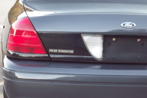 2001 Ford Crown Victoria - The rear of a dark gray 2001 Ford Crown Victoria Police Interceptor is visible, showing the taillight and reverse light.