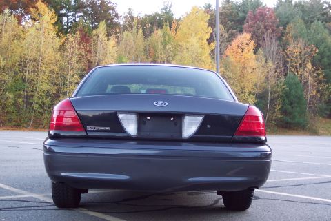 2001 Ford Crown Victoria - Rear view of a dark 2001 Ford Crown Victoria, identified by its distinctive taillights and 'Police Interceptor' badging.