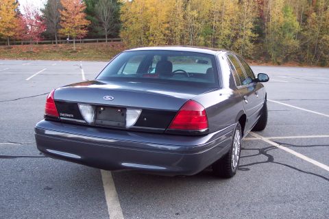 2001 Ford Crown Victoria - Rear view of a Ford Crown Victoria parked in an empty lot with autumn trees in the background.