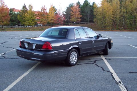 2001 Ford Crown Victoria - This 2001 Ford Crown Victoria is shown from the rear three-quarter angle in a parking lot with autumn trees in the background.