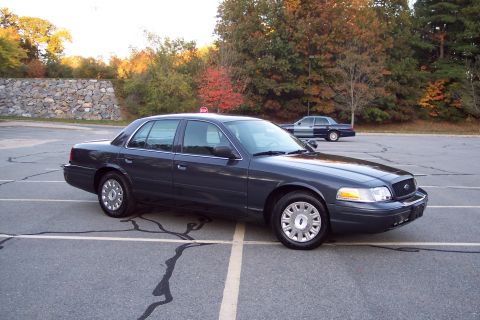 2001 Ford Crown Victoria - A dark gray 2001 Ford Crown Victoria is parked in a lot, with another vehicle visible in the background.