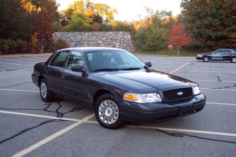 2001 Ford Crown Victoria - A dark gray Ford Crown Victoria is parked in a lot with autumn trees in the background.