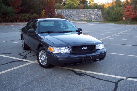 2001 Ford Crown Victoria - A dark gray 2001 Ford Crown Victoria sedan is parked in an empty lot on a sunny day.