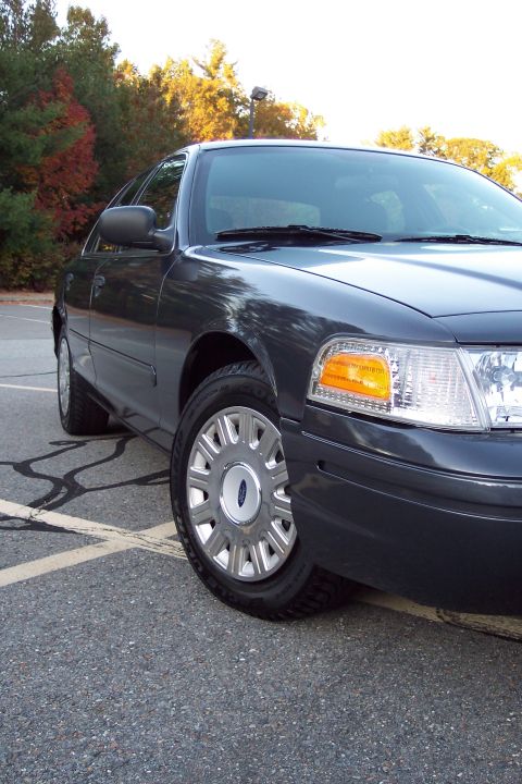 2001 Ford Crown Victoria - A dark gray Ford Crown Victoria is parked in a lot with trees in the background.