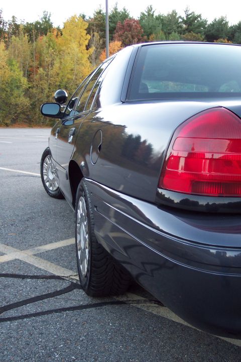 2001 Ford Crown Victoria - Rear view of a dark 2001 Ford Crown Victoria parked on asphalt with trees in the background.