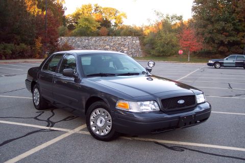 2001 Ford Crown Victoria - A dark gray 2001 Ford Crown Victoria is parked in a lot with another vehicle in the background.
