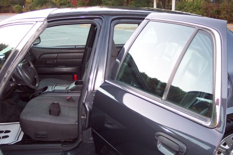 2001 Ford Crown Victoria - Interior view of a dark sedan, likely a 2001 Ford Crown Victoria, with both front and rear doors ajar.