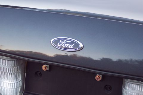 2001 Ford Crown Victoria - Close-up of the Ford emblem on the trunk of a dark gray vehicle, showing part of the taillight assembly.