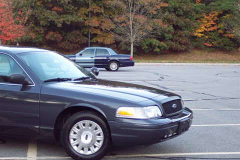 2001 Ford Crown Victoria - Two Ford Crown Victorias parked in a lot during autumn. The foreground car is dark gray.