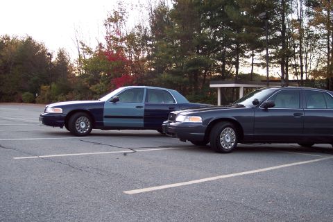 2001 Ford Crown Victoria - Two Ford Crown Victoria police cars are parked in a lot. One has a two-tone paint job.