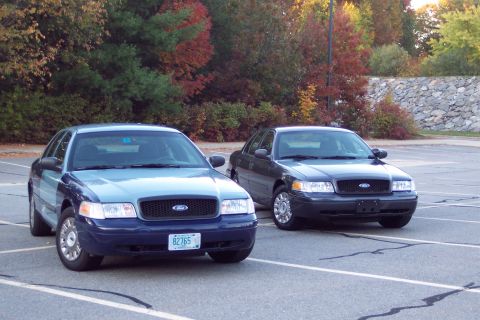 2001 Ford Crown Victoria - Two Ford Crown Victorias are parked side-by-side in a parking lot, with autumn foliage in the background.