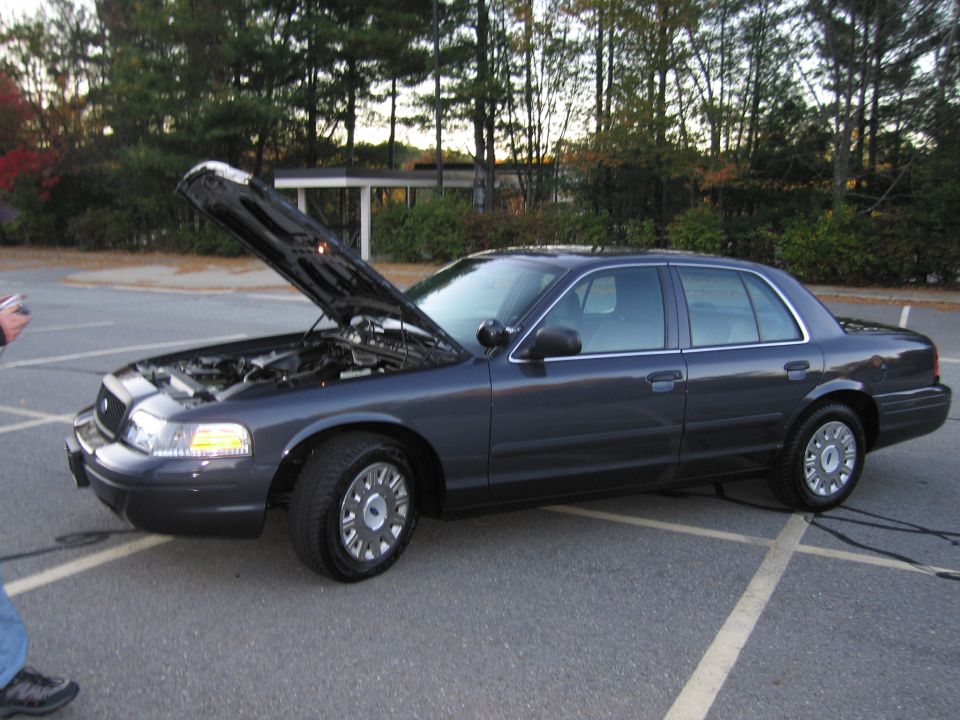 Photo of a gray Ford Crown Victoria sedan with hood open in a parking lot
