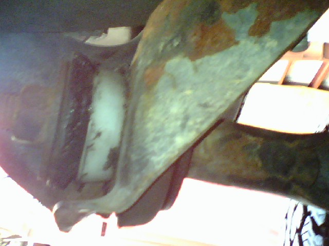 Underside of a vehicle showing rusty metal and a white plastic component.