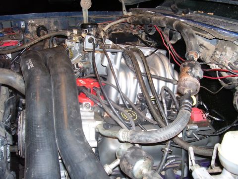 1991 Ford Bronco - The image shows a close-up view of a blue Ford Bronco's engine bay, focusing on the intake manifold, hoses, and various engine components.…