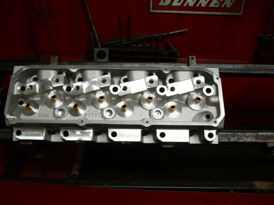 Overhead view of a machined aluminum cylinder head with brass valve guides and rocker arm studs.