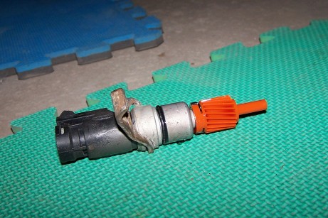 2000 Ford Crown Victoria - A vehicle speed sensor with an orange gear is shown lying on a green interlocking mat. The sensor has a black plastic connector and a metal…