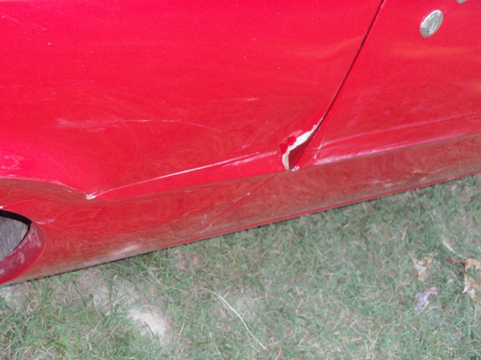 Close-up of crumpled red rocker panel and torn lower door edge with exposed bare metal