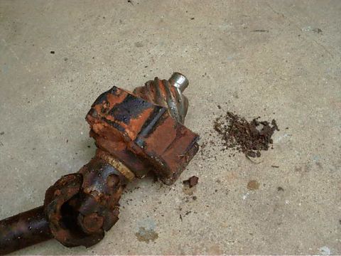 1985 Ford Bronco - A heavily rusted driveshaft component lies on a concrete surface next to a pile of debris.