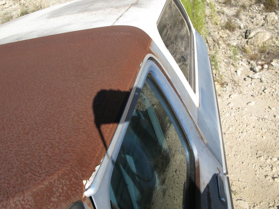 Heavily rusted brown roof and blue door of a classic vehicle with a white roof.