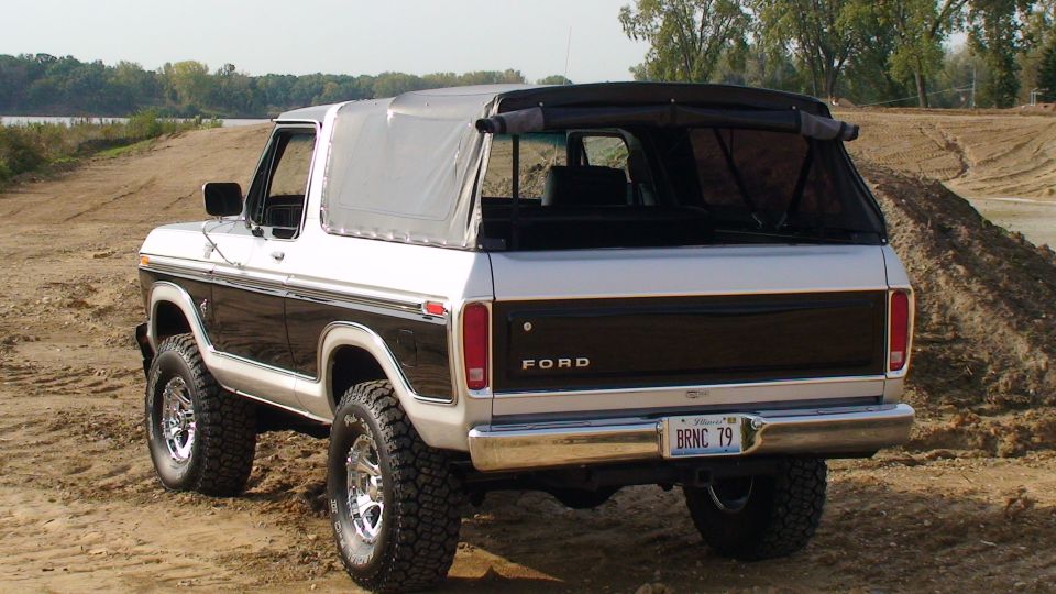 1979 Ford Bronco with a soft top, silver and black paint, parked on a dirt lot.