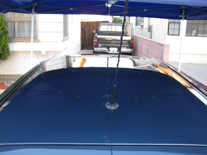 Dark blue car roof with antenna, black pickup truck in background under canopy.