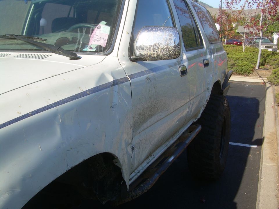 Driver's side of muddy white 4Runner with crushed rocker panel and dented door above rock slider