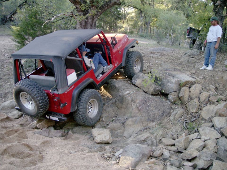 Red Jeep CJ flexing over rocks on an off-road trail