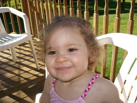 2000 Ford Crown Victoria - A young child with curly brown hair smiles while sitting on a white plastic chair on a wooden deck. The child is wearing a pink tank top wi…