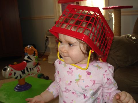 2000 Ford Crown Victoria - A young child wears a red plastic basket on their head while sitting in a room with toys.