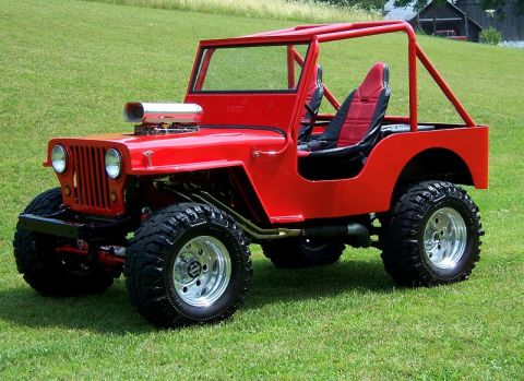 1948 Jeep Wrangler - A bright red, heavily modified Jeep CJ-2A is parked on a grassy lawn with a building in the background. This custom Jeep features a promine…
