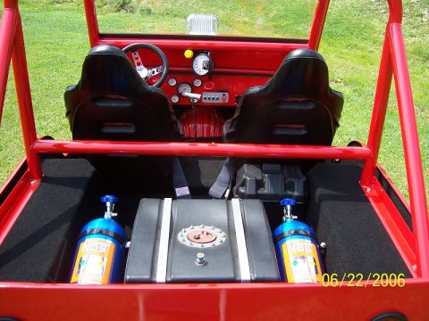 1948 Jeep Wrangler - The interior of a red custom off-road vehicle is shown from a rear-facing perspective, featuring two black racing seats, a dashboard with g…