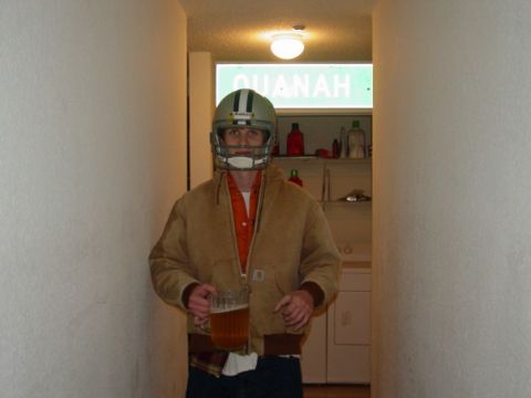 1983 Ford F-250 - A man in a football helmet and jacket holds a beer mug in a hallway with a street sign overhead.