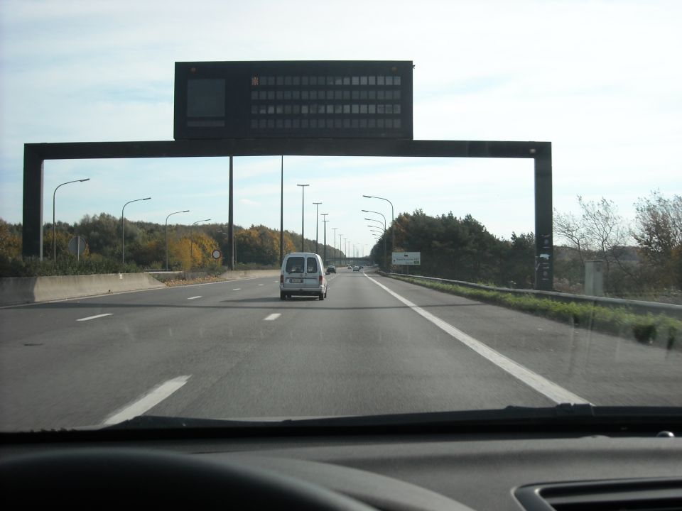White van driving on a highway under a large overhead sign