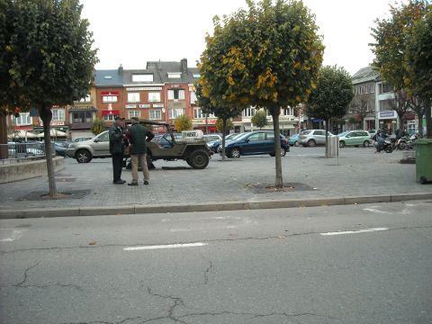 1979 Ford F-150 - A vintage olive green jeep is parked in a town square, with two men standing beside it. Other vehicles and buildings are visible in the bac…