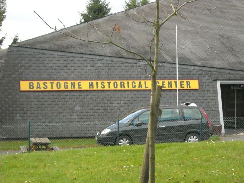 1979 Ford F-150 - A dark minivan is parked outside the Bastogne Historical Center, a building with a large yellow sign.