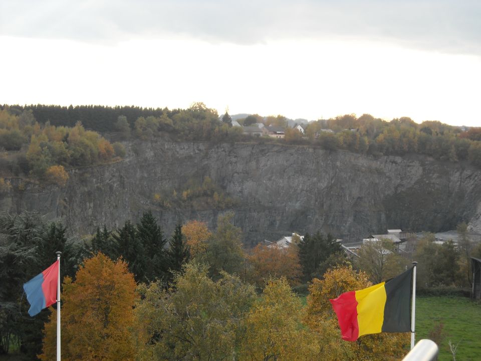 Belgian flag and another flag fly in front of a quarry with trees in autumn colors