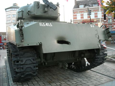 1979 Ford F-150 - A military tank with battle damage is displayed outdoors on a paved surface.