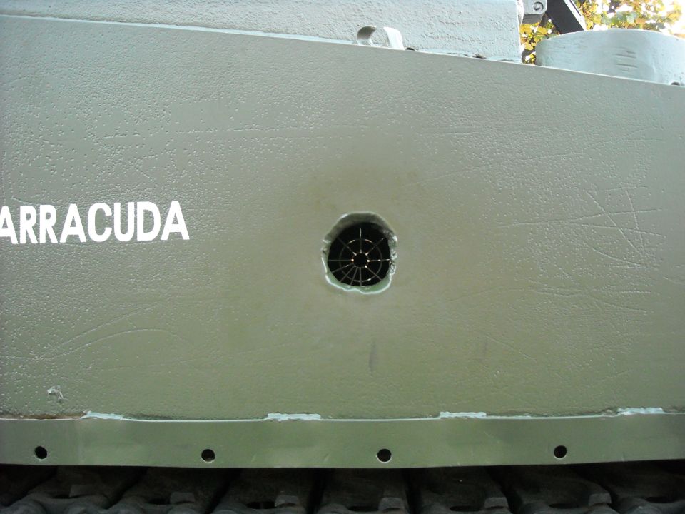 Close-up of a green military vehicle side panel with the word ARRACUDA stenciled on it and a circular vent