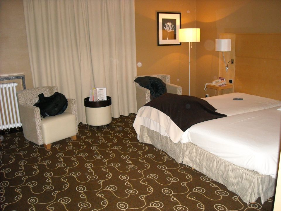 Hotel room with two beds, armchair, side table, and radiator