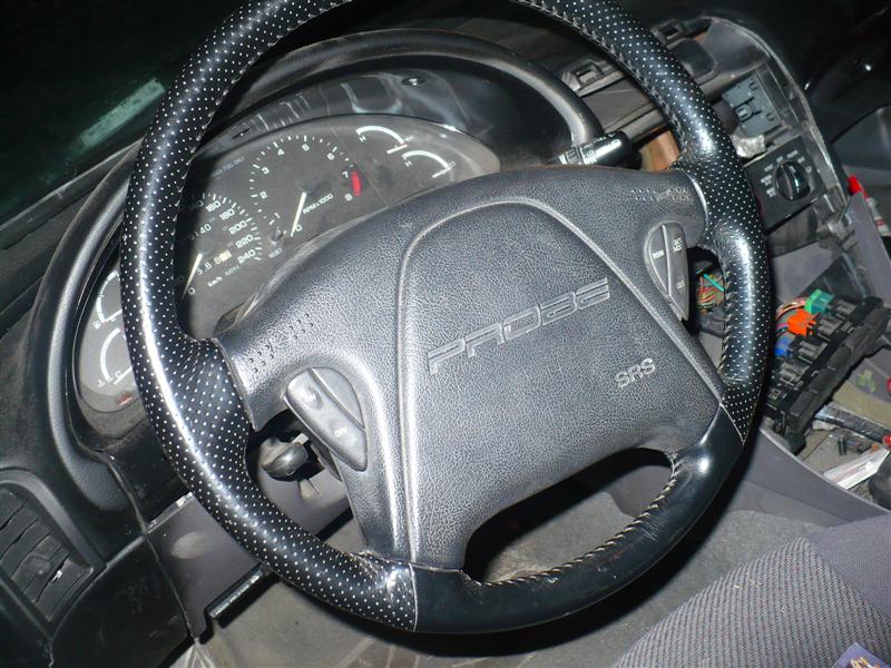 Interior shot of a car's steering wheel with 'PROBE' embossed on the airbag cover. Dashboard gauges are visible