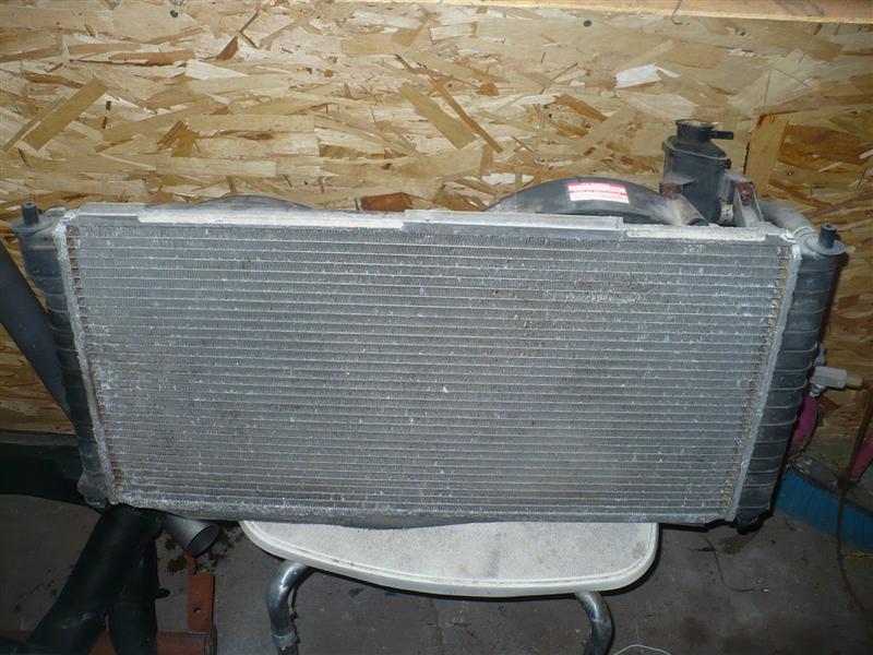 Car radiator with fans and hoses, sitting on a chair in front of a wood-paneled wall